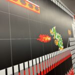 Long wall mural with large black tiles and a red-and-white checkered border, featuring pixel art characters from classic arcade games on the right side