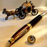 Ornate brass horse-drawn carriage statue with decorative wheels on a beige surface beside a long black-and-gold lacquered object.